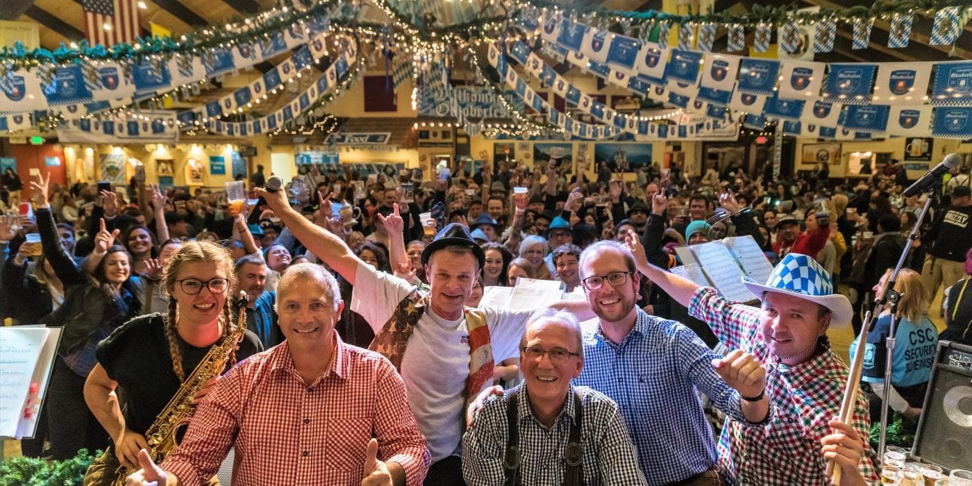 A band on stage before a packed crowd under blue-and-white Bavarian bunting at Big Bear Oktoberfest